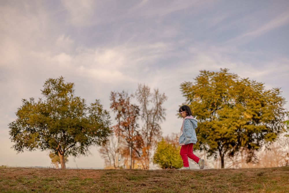 Low-angle wide shot of young girl walking along a sidewalk, framed by grassy hill and open sky—candid outdoor moment in Escondido, CA.