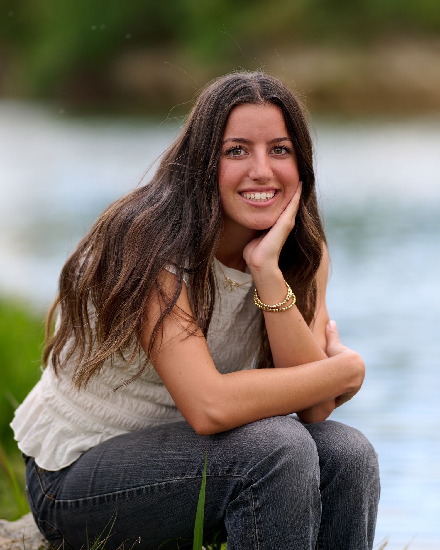Person poses on rocks near water in casual outfit during outdoor portrait session at sunset.