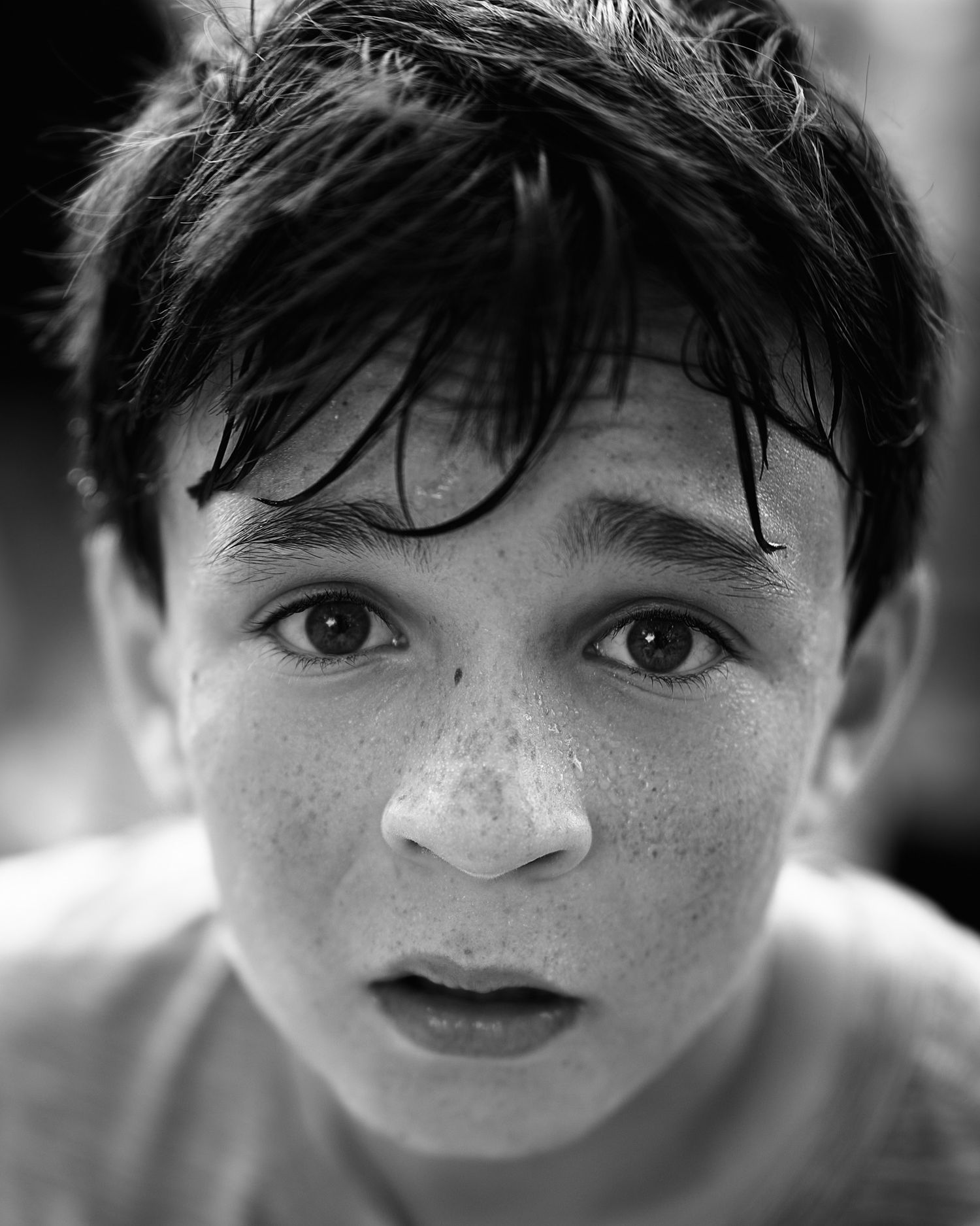 A black and white close-up portrait showing freckles and wet hair against a blurred background.