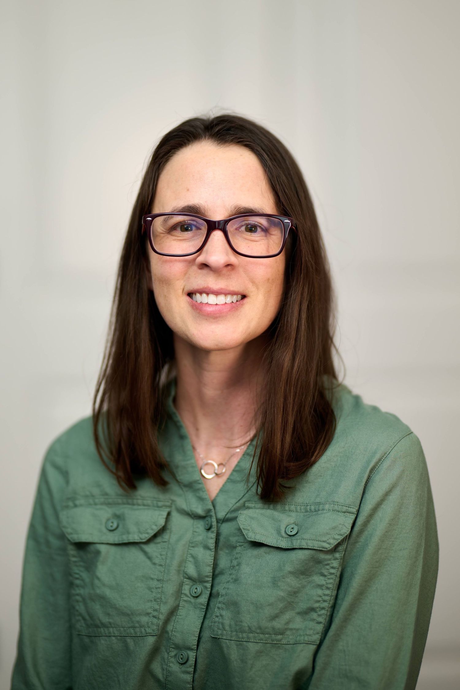 Portrait of a smiling person wearing glasses and a green button-up shirt.