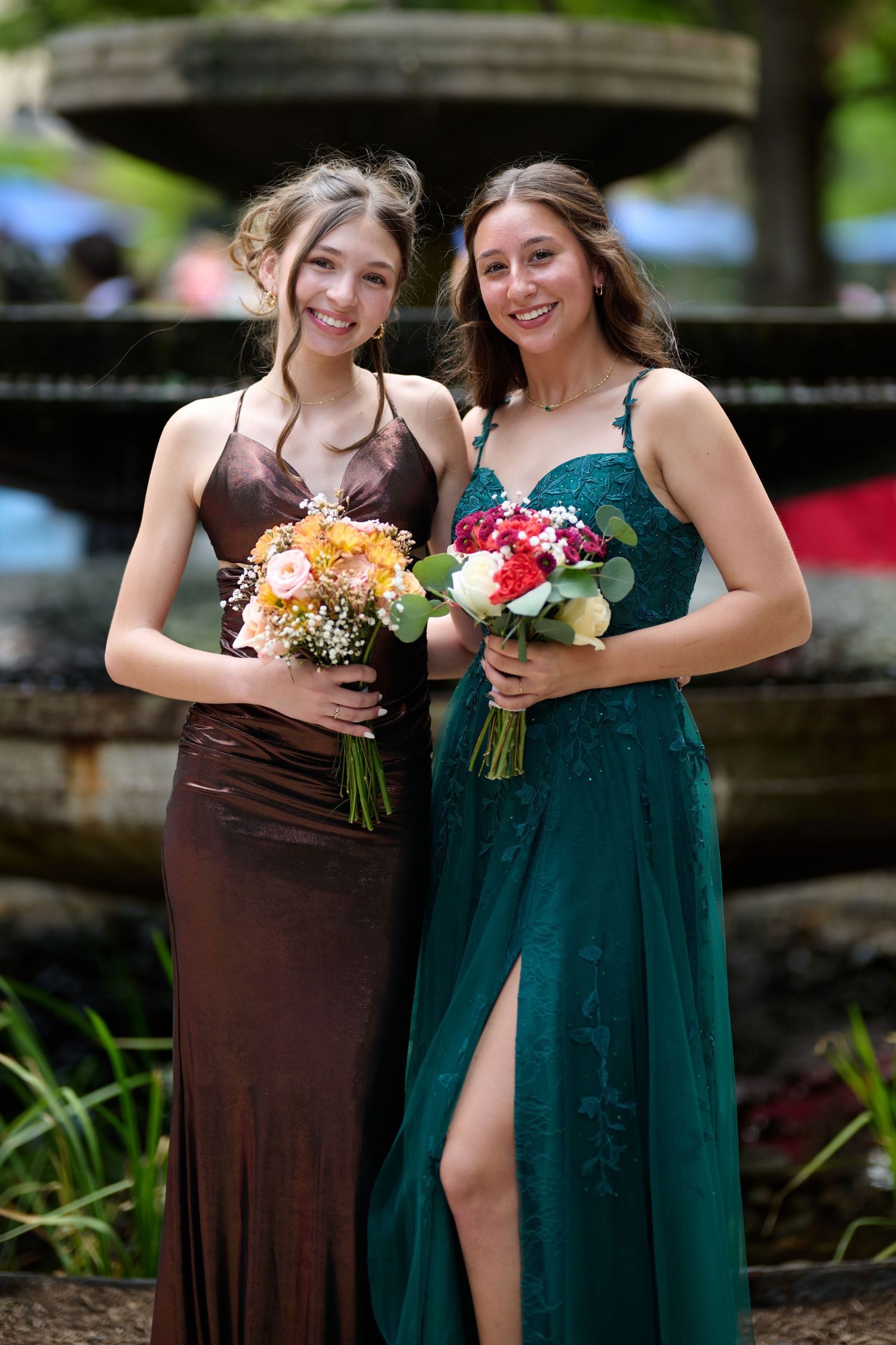 Two attendants in formal dresses hold colorful floral bouquets at an outdoor event.