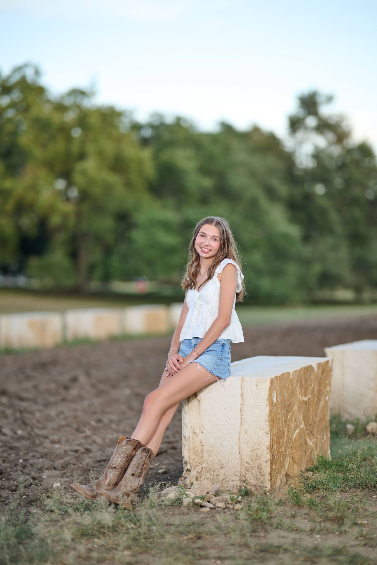 Casual summer portrait of someone sitting on concrete wall wearing boots and denim shorts.