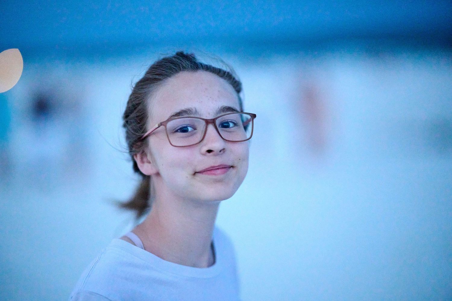 A portrait in soft blue lighting showing a student wearing glasses.