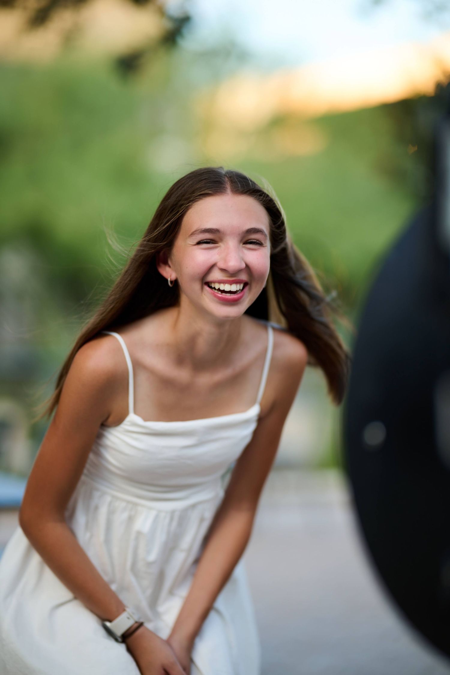 Young person in a white summer dress laughing joyfully outdoors at sunset.