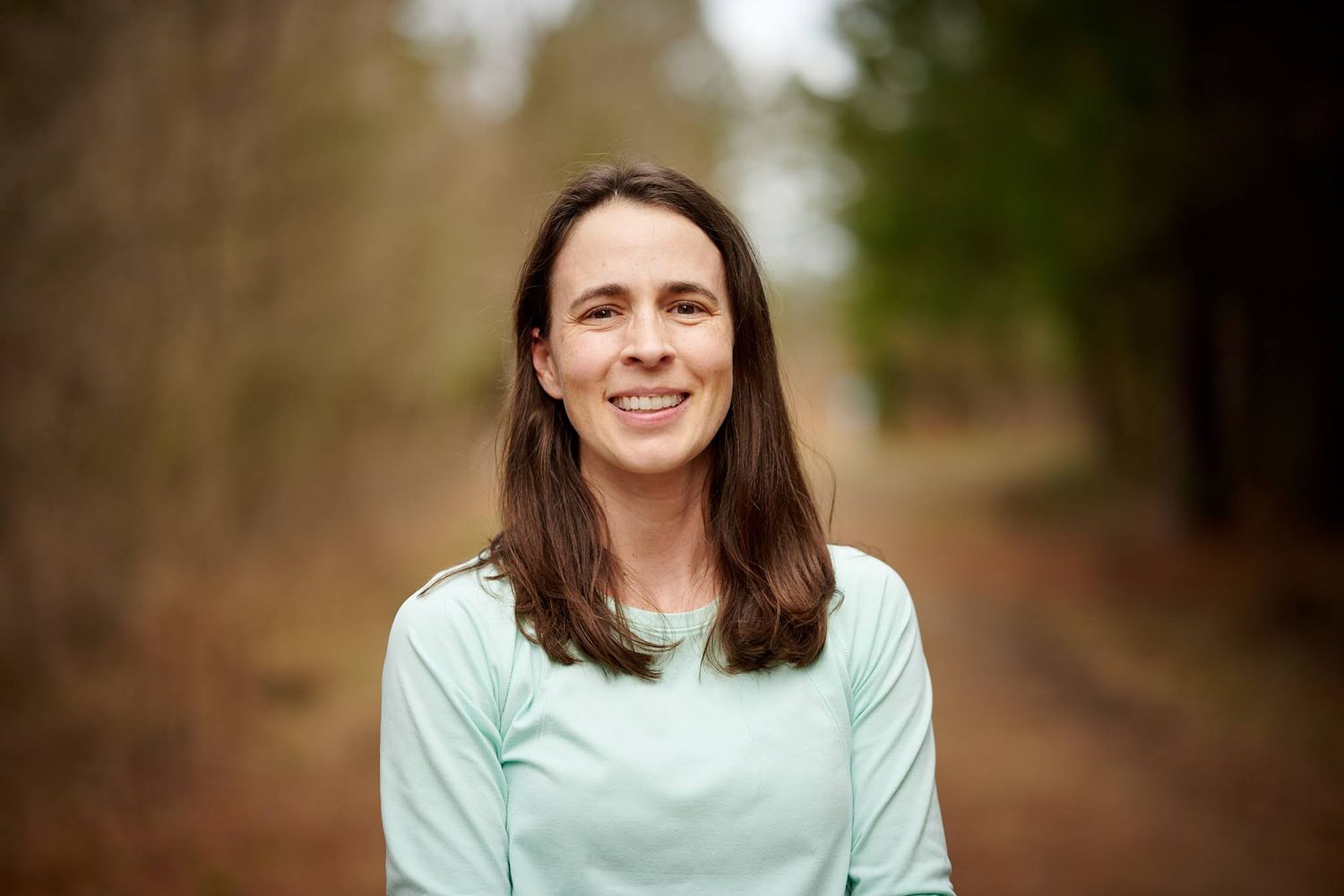 Casual portrait of a person in mint green top smiling on a wooded path.