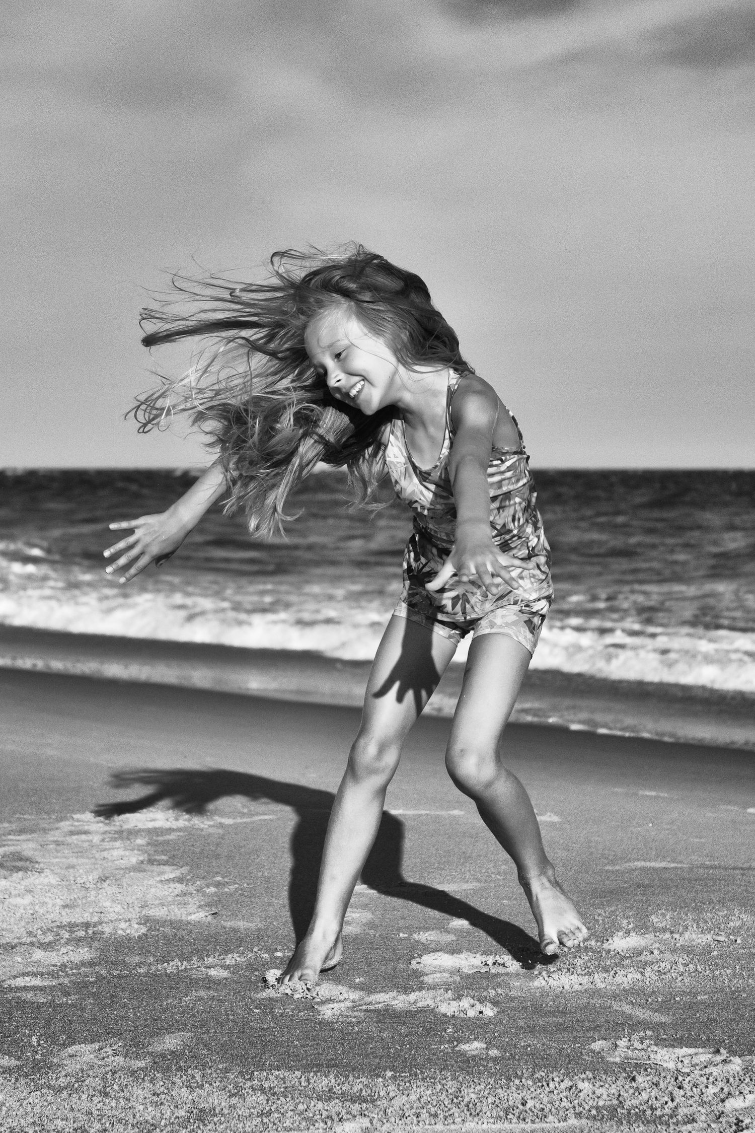 Black and white image of people playing and running along beach shoreline.