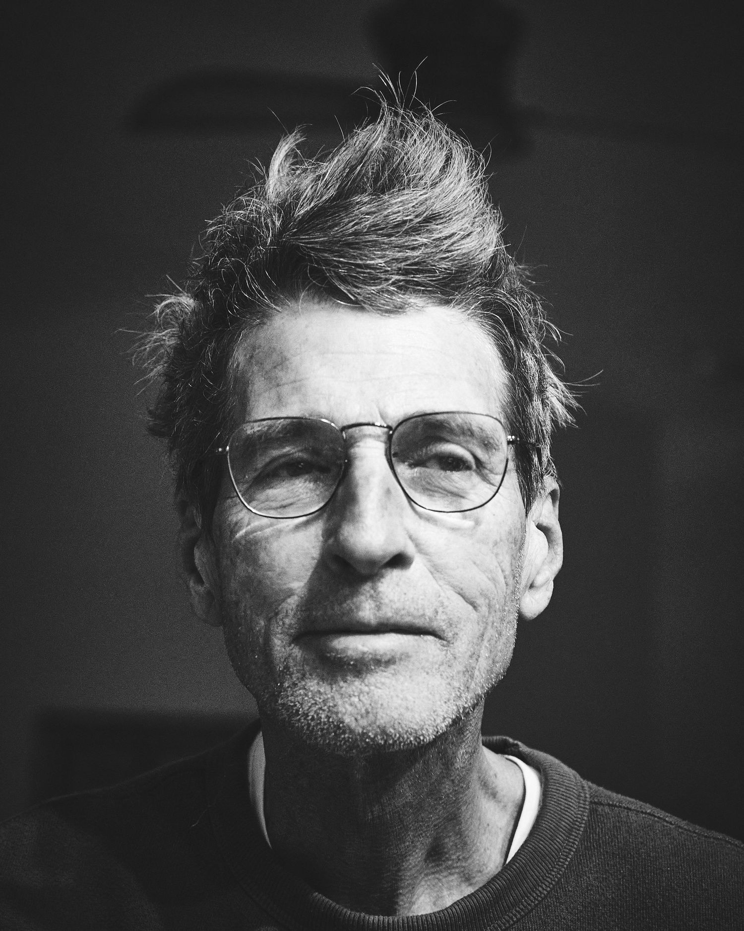 Dramatic black and white headshot featuring glasses and tousled hair against dark background.