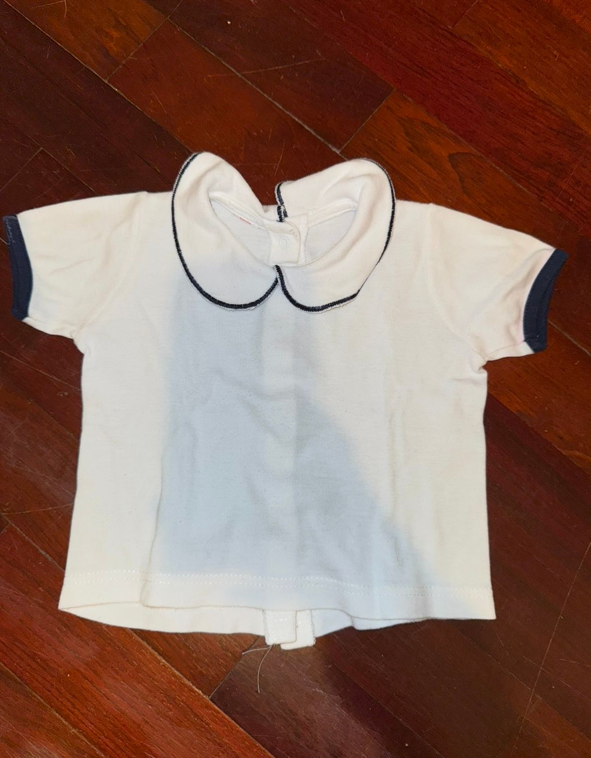 White peter pan collar baby blouse laid flat on wooden floor showing different angles.