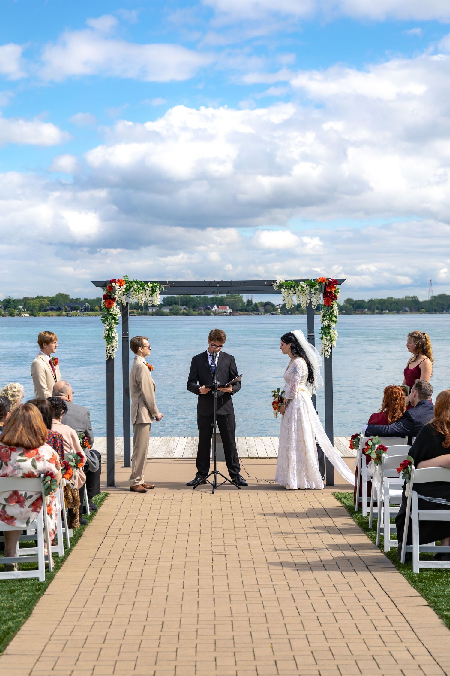 A bride and groom at the alter during their wedding at St Clair Inn, with floral arch and white chairs overlooking the waterfront.