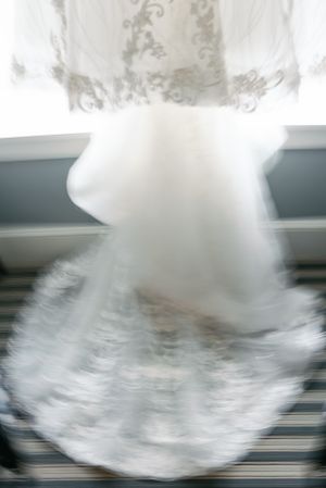 An artistic blurred close-up shot of a white wedding dress skirt with delicate lace detailing.