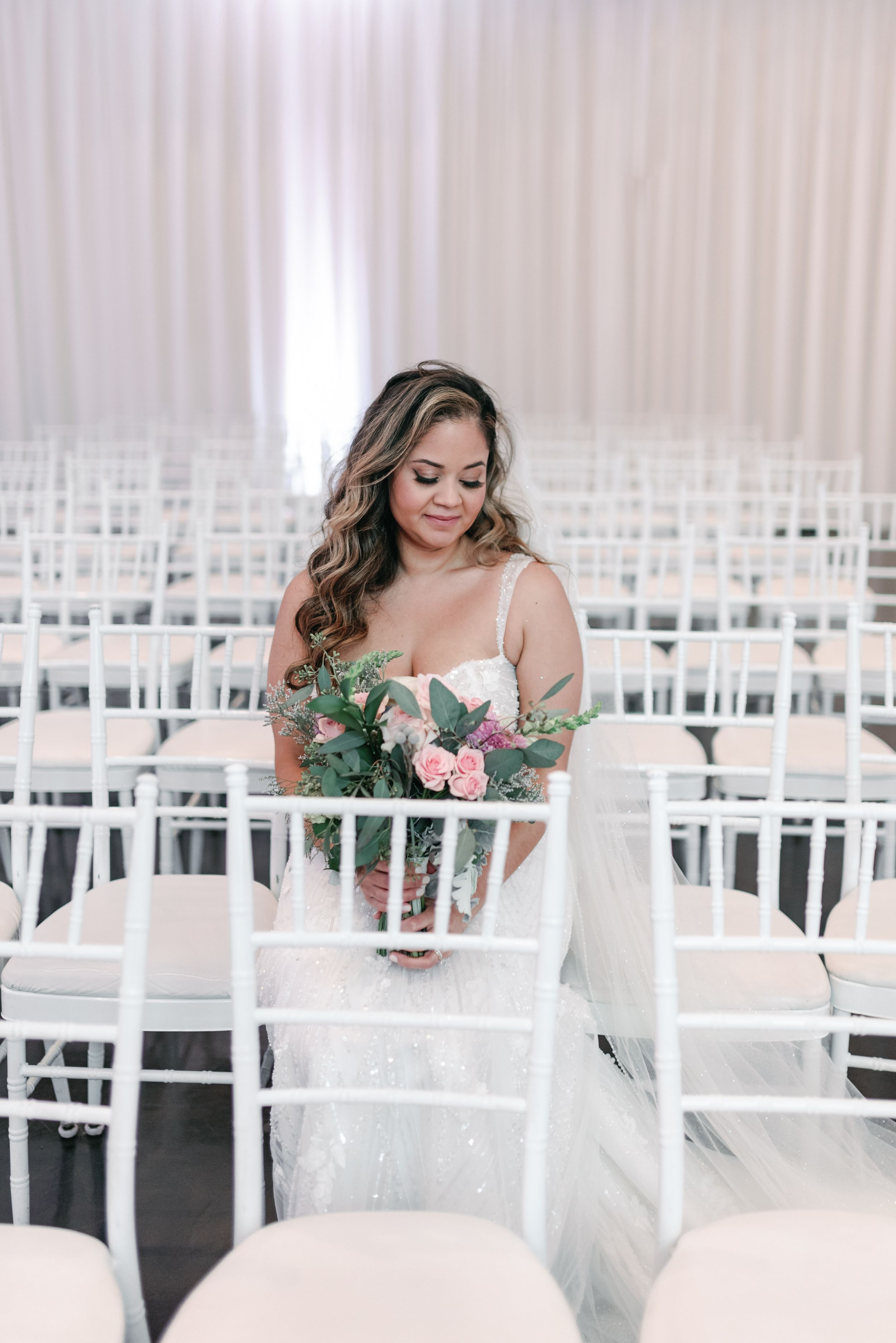 An elegant wedding ceremony setup with white chairs and floral decorations in a light-filled room.