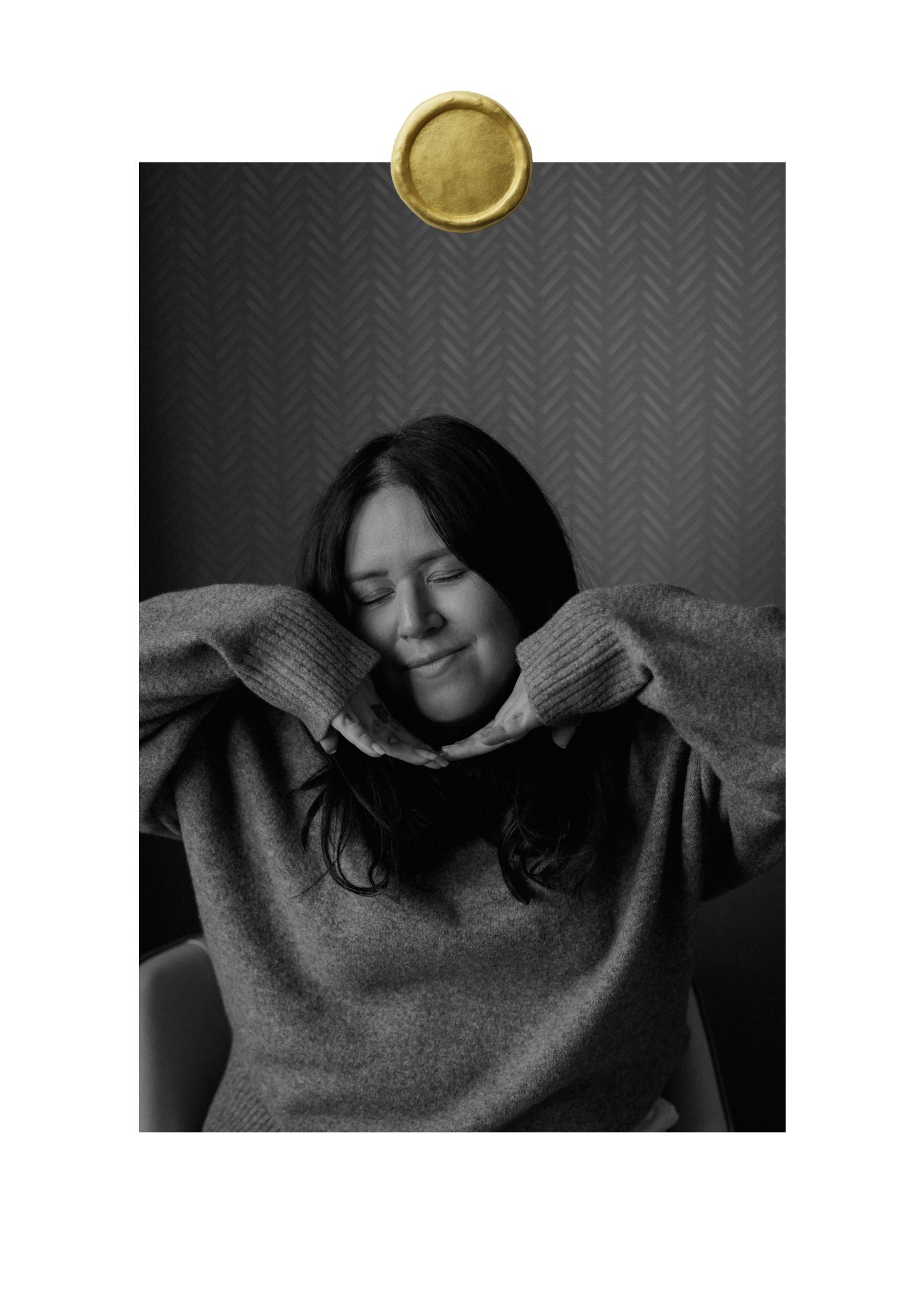 A black and white portrait of someone in a cozy sweater with closed eyes and a gentle smile against a textured wall.