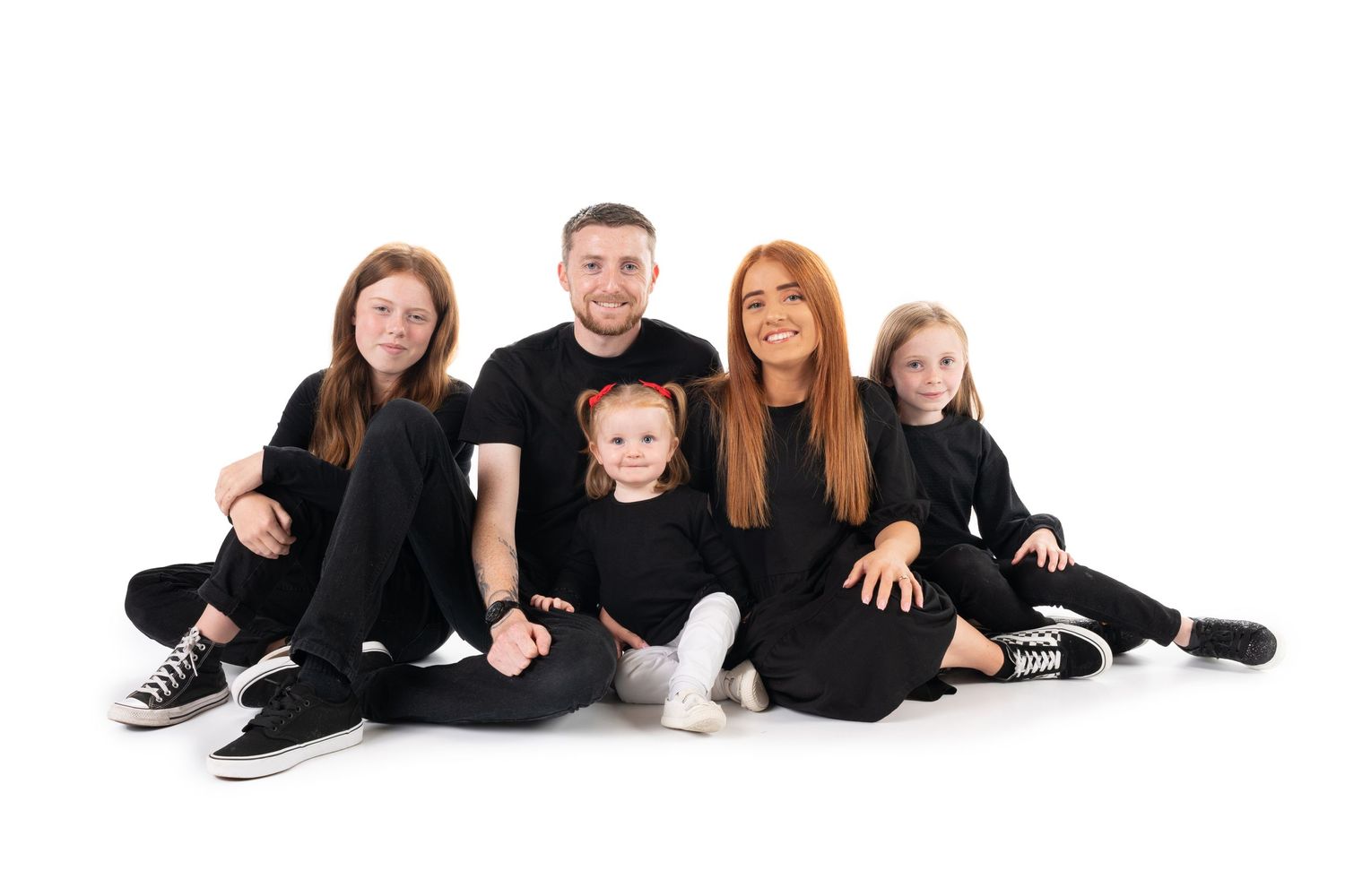Family of five wearing matching black outfits poses against white background.