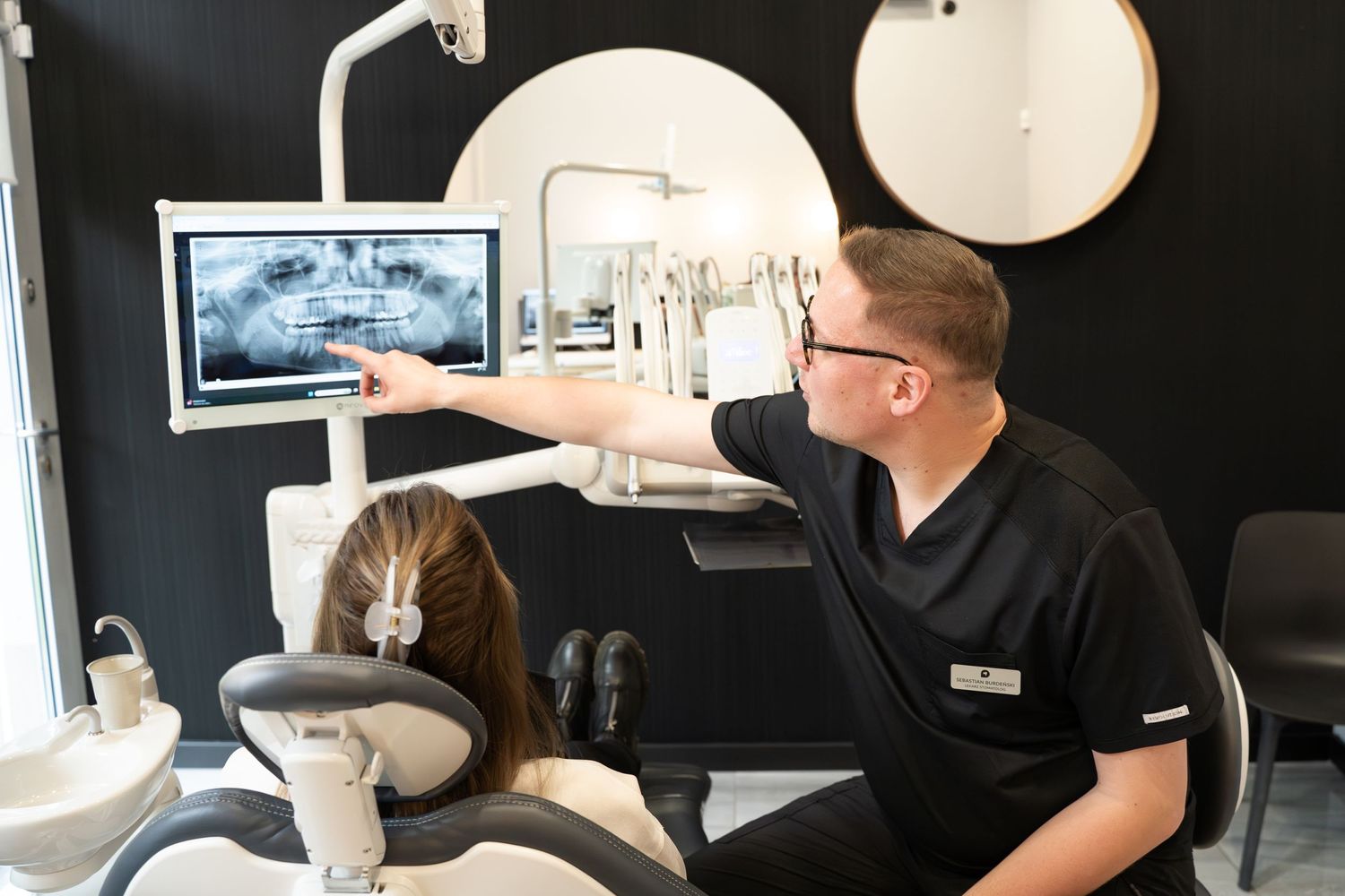 Dentist pointing to digital display while consulting in modern dental office.