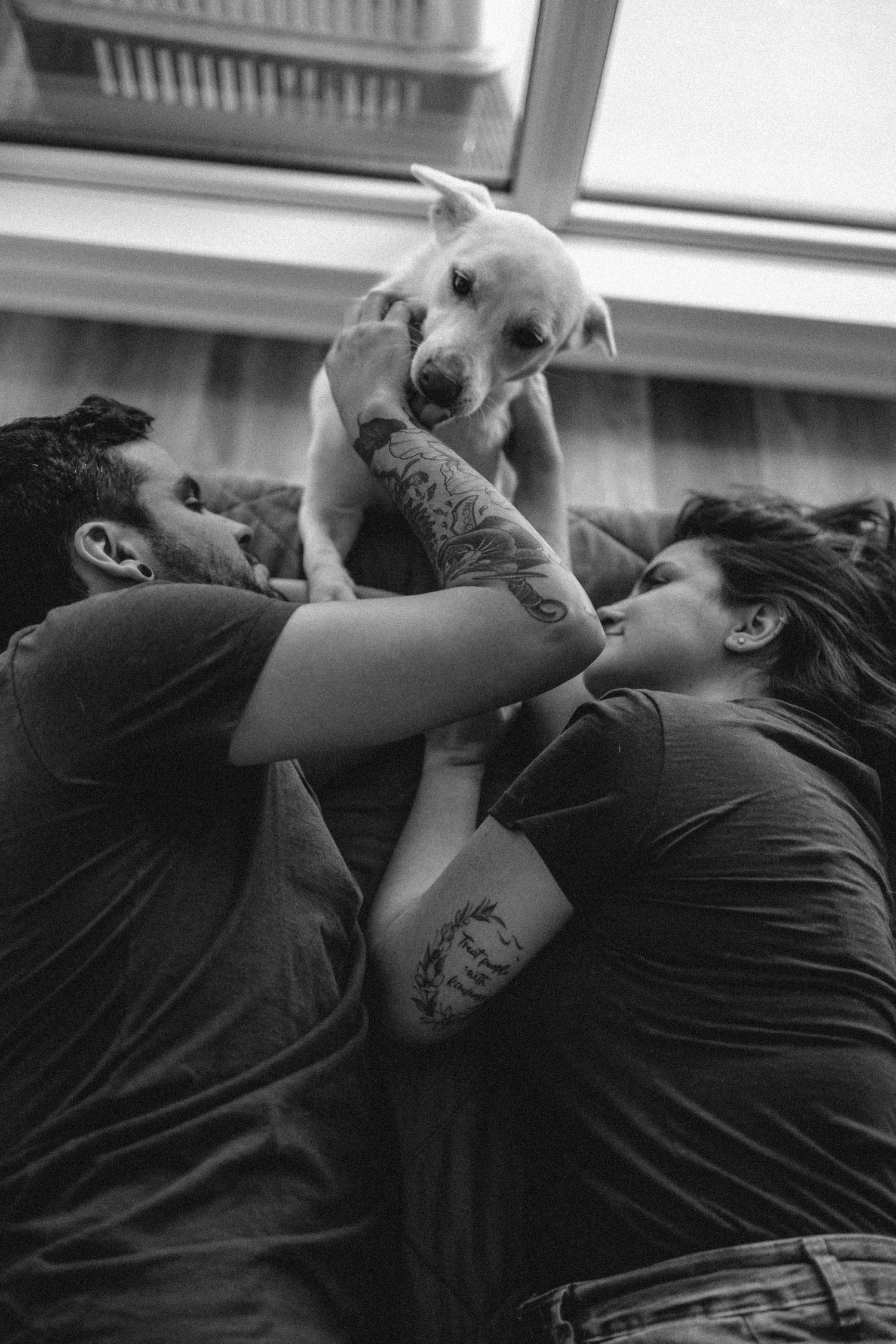 couple on the bed playing with their white dog that is on the floor