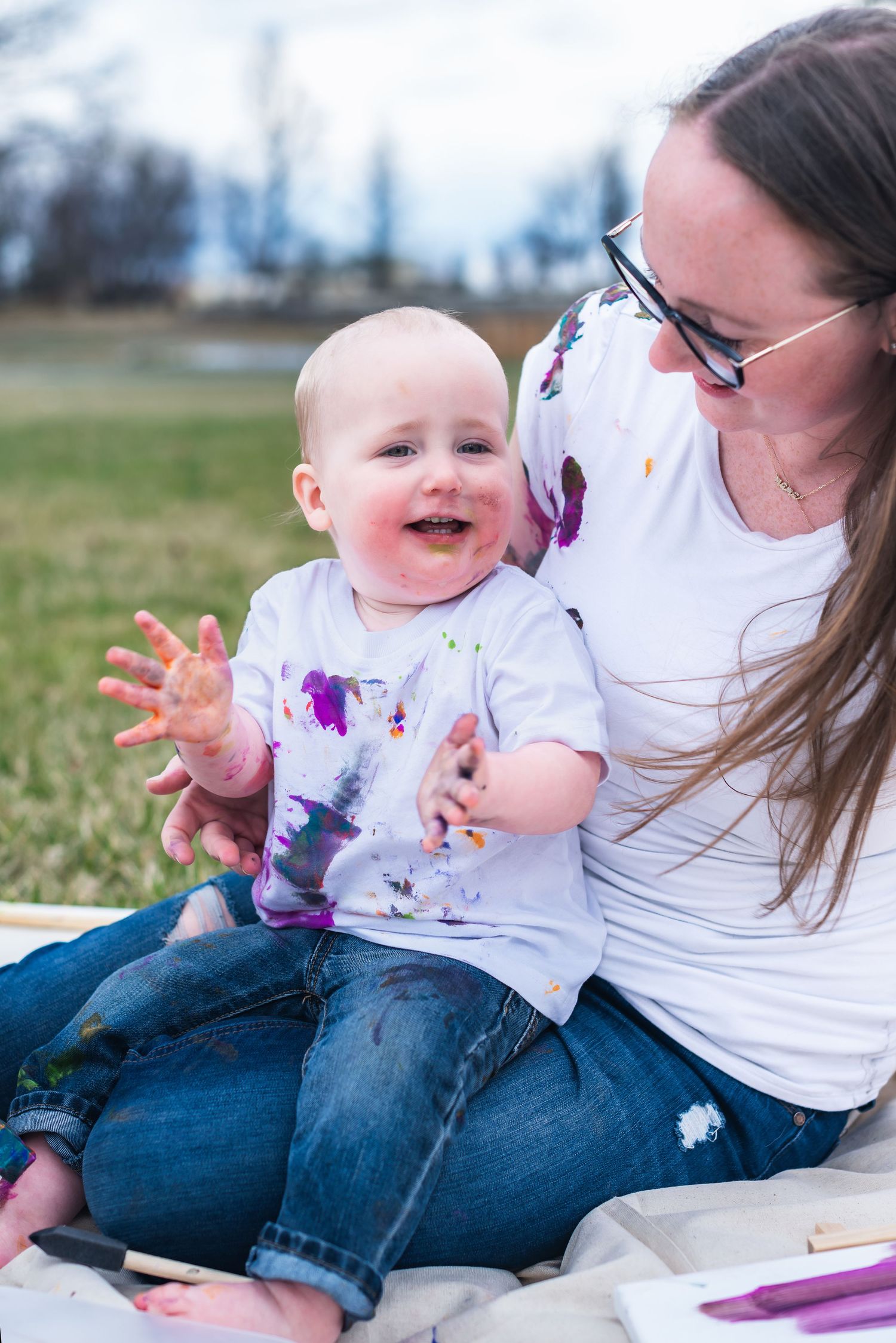A joyful moment shared between parent and child sitting outdoors with matching paint-splattered white shirts.