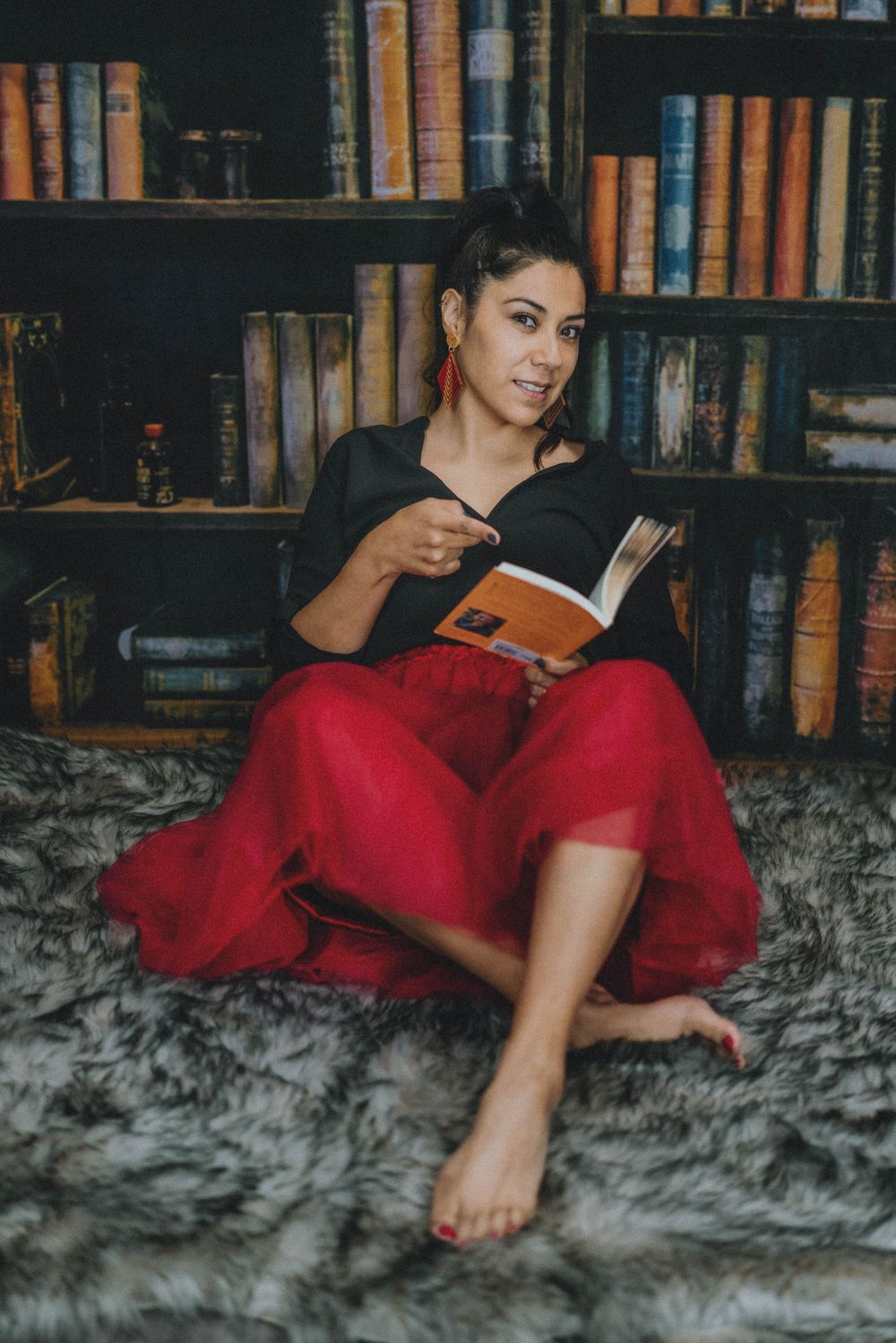 Someone reading a book while relaxing on a fur rug in front of a bookshelf.