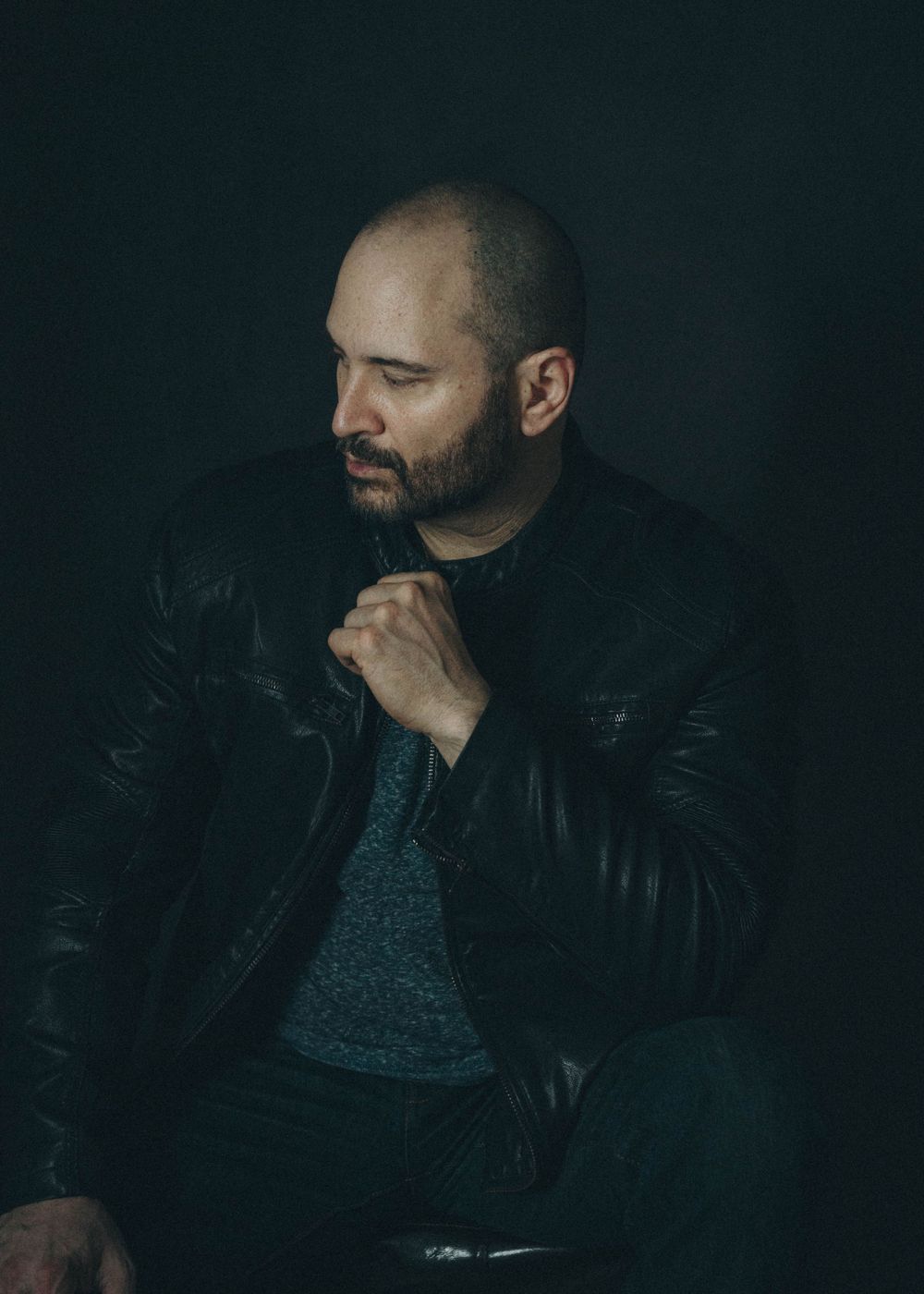 Dramatic profile portrait of someone in a leather jacket against dark background with moody lighting and thoughtful pose.