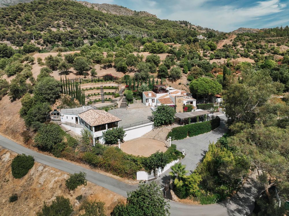 Aerial view of Spanish hillside villa with terraced gardens and Mediterranean architecture nestled among olive trees in rural setting.