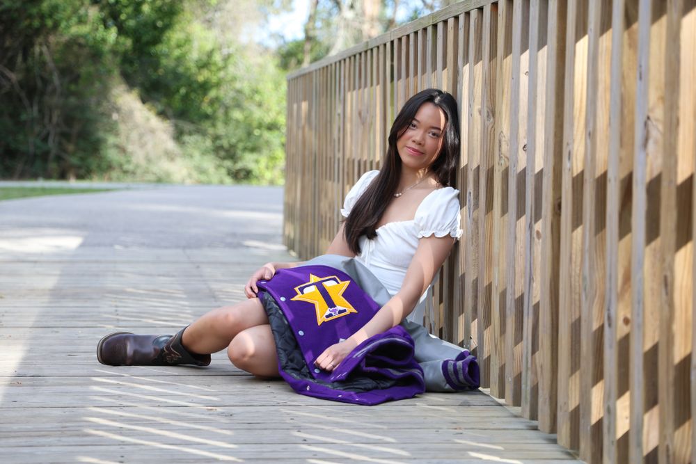 Casual outdoor photos on a wooden bridge featuring purple varsity jacket and white dress.