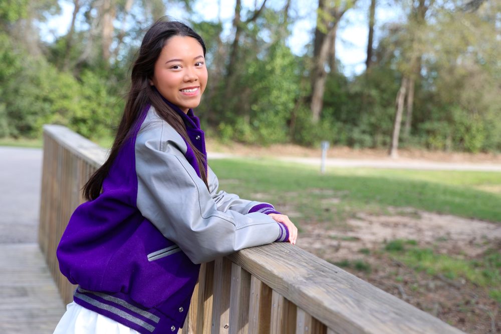 Athletic wear photoshoot featuring purple varsity jacket in natural outdoor setting.