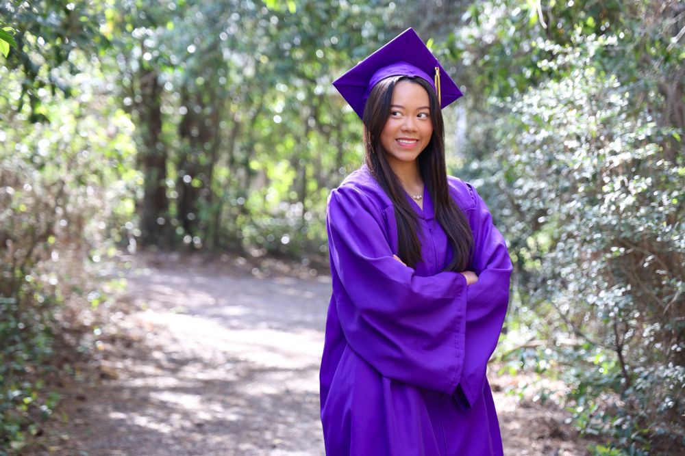 Outdoor portrait series in purple graduation attire surrounded by trees and foliage.