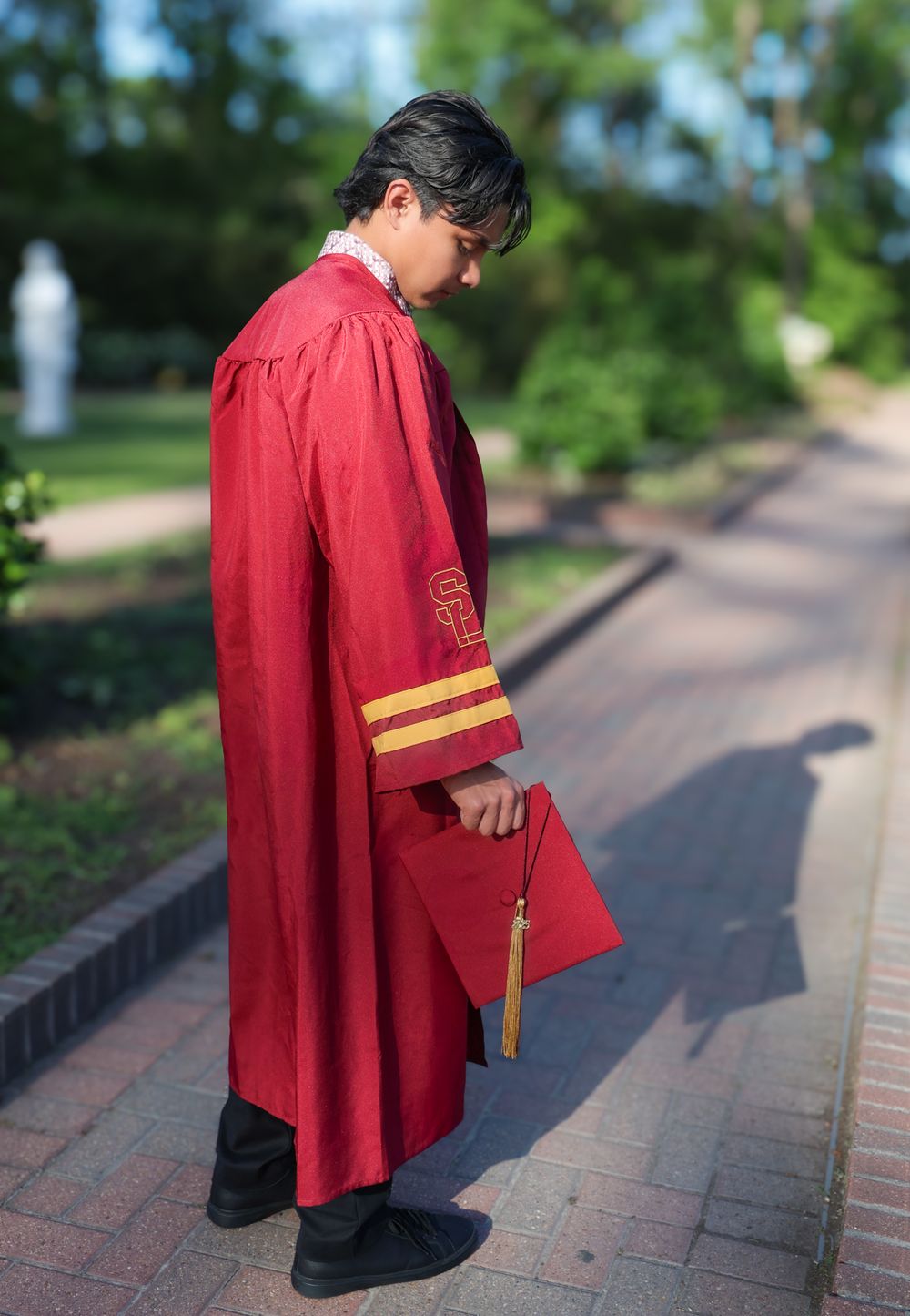 Close-up details of burgundy graduation gown with gold stripes on pathway.