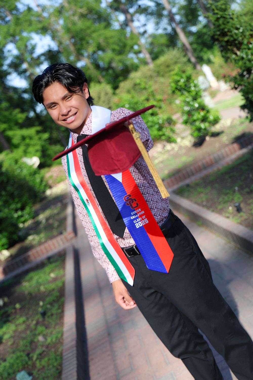 Graduate wearing stoles representing different countries poses on brick walkway.