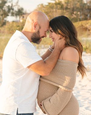 Intimate maternity photoshoot of couple embracing on sandy beach at sunset.