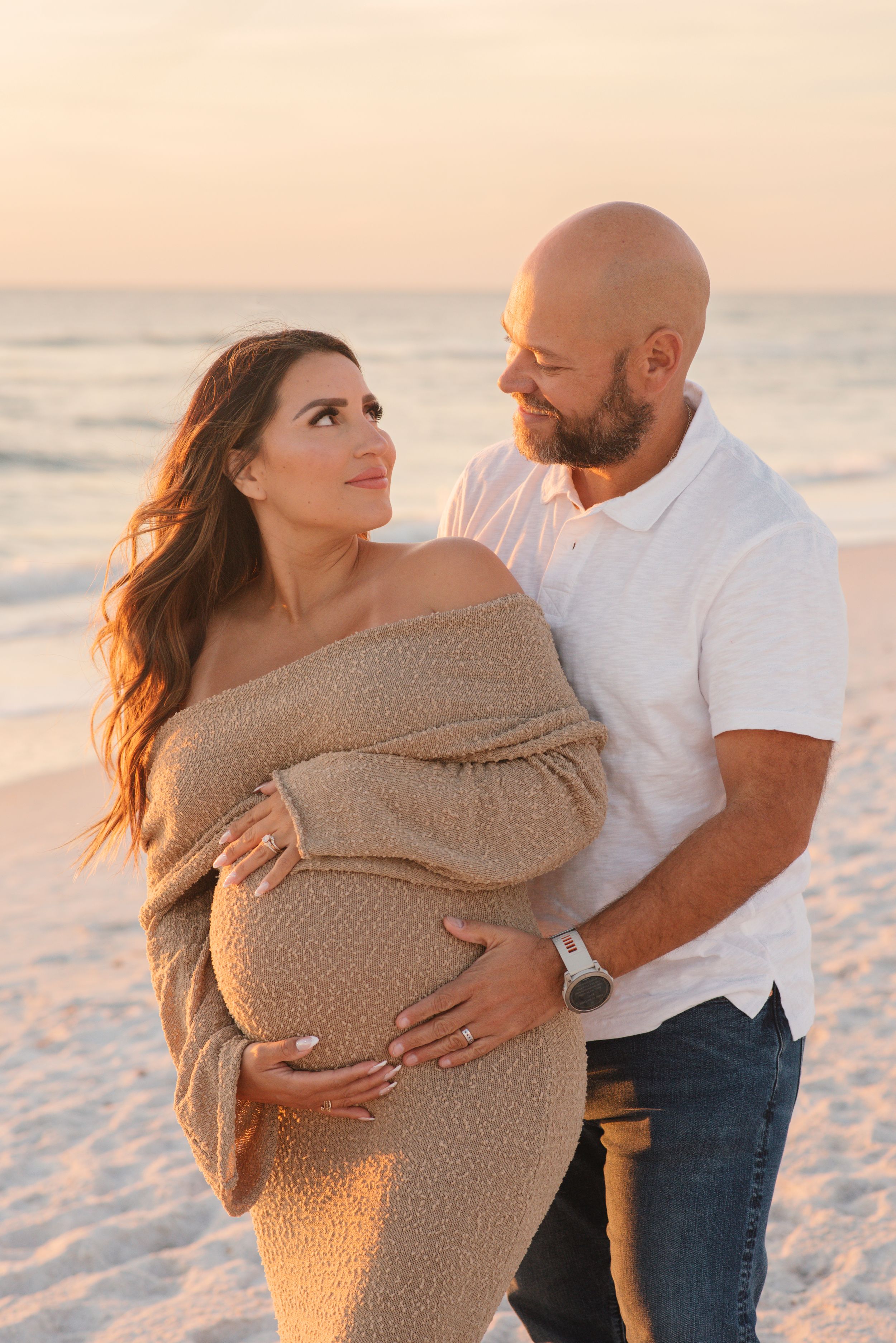 Romantic maternity photo of couple embracing on beach during golden hour.