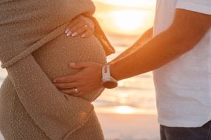 Close-up of hands gently cradling a pregnant belly during a golden hour beach photoshoot.
