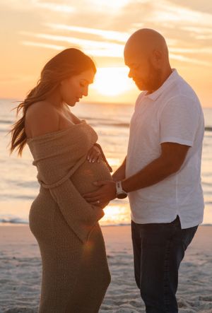 A tender maternity photoshoot silhouette at sunset on the beach with the expectant mother in a cozy sweater.