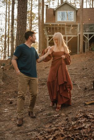 A couple walking together near a rustic treehouse in the woods at sunset.