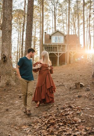 A romantic moment between a couple by a treehouse with sunlight filtering through pine trees.