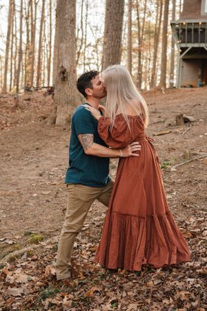 A romantic couple embracing on fallen leaves near a treehouse in the forest.