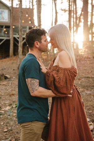 A tender moment between a couple in front of a rustic treehouse during sunset.