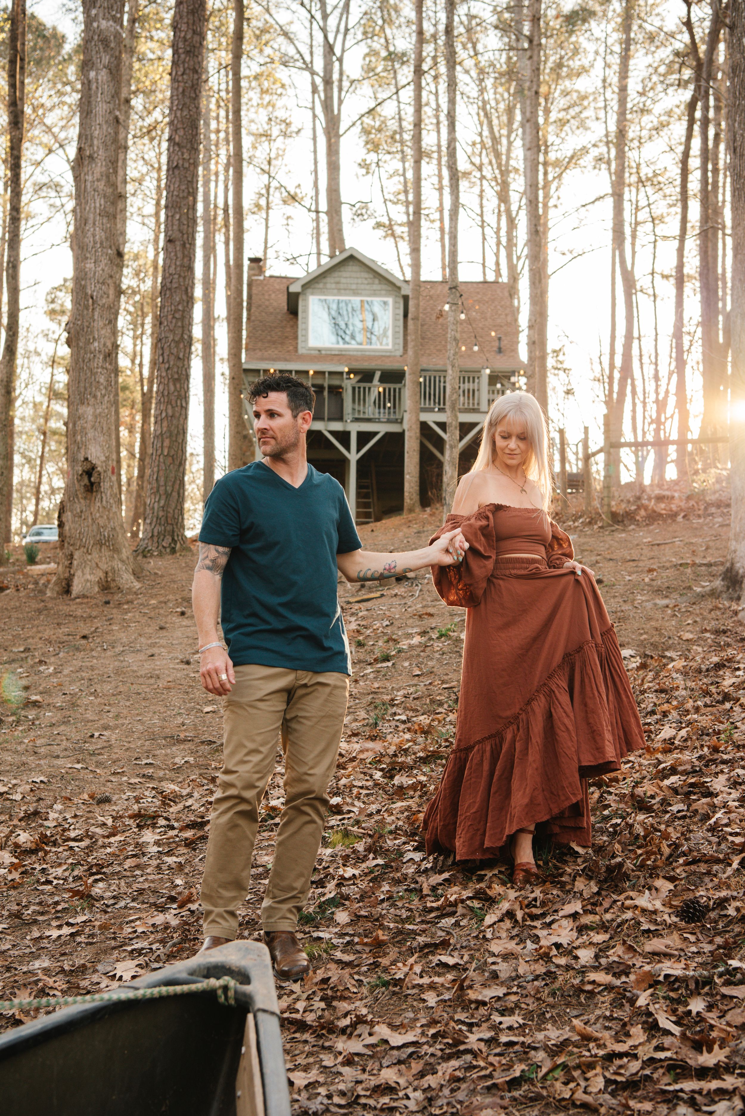 A couple in casual attire walking near their treehouse during golden hour in the woods.