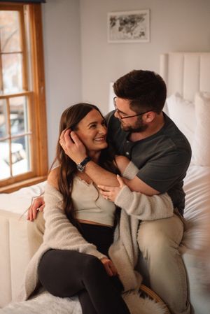 A cozy intimate moment between a couple lounging together on a white couch by a window.