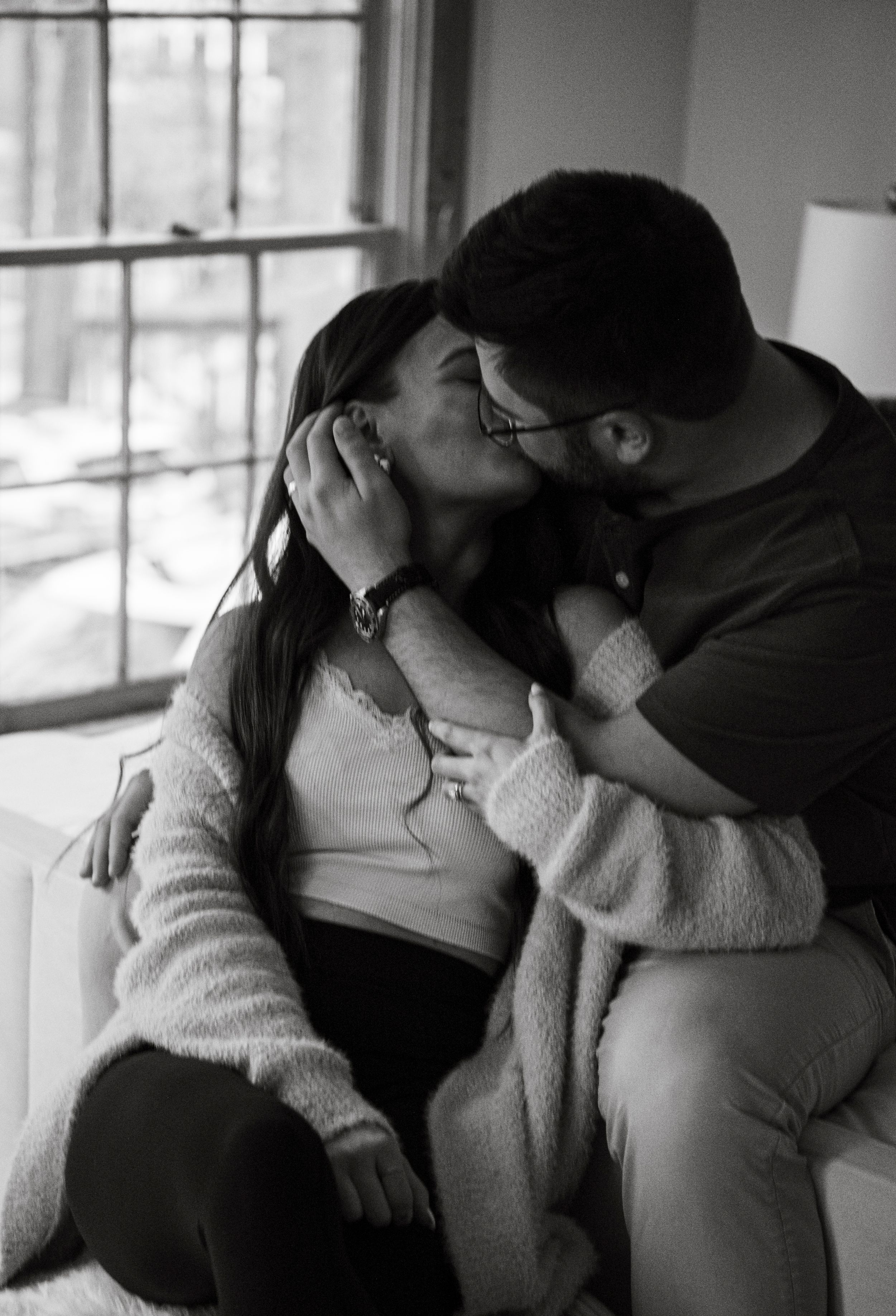 Intimate black and white photo of couple sharing tender moment by window.