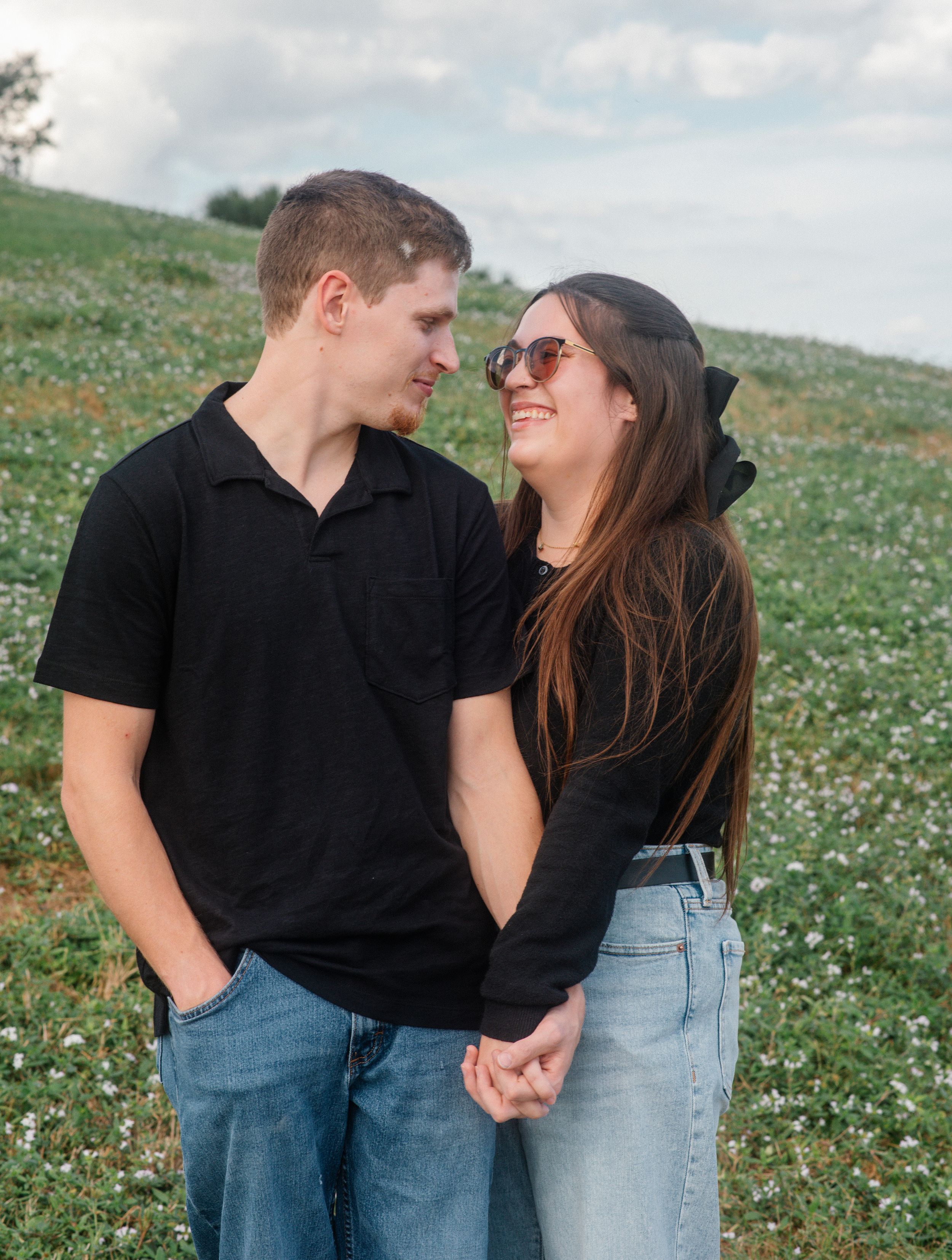 A romantic couple shares a tender moment while holding hands in a flower-dotted meadow at sunset.