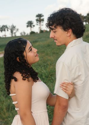 A couple gazes lovingly at each other in an outdoor setting with palm trees in the background.