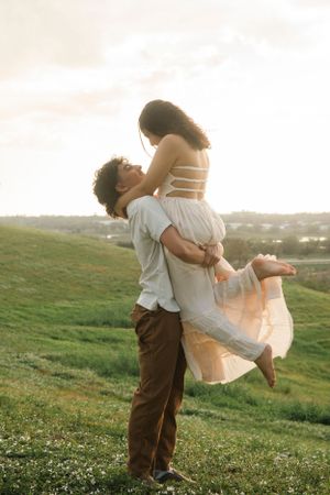 A romantic lift pose captured in golden hour light on a grassy hillside.