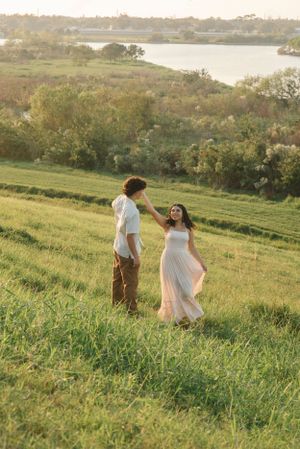 A couple in casual attire stands together on a hill during golden hour with a lake in the background.