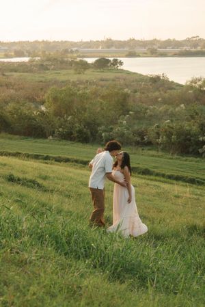 A romantic moment between two people on a hillside at sunset with water visible in the distance.