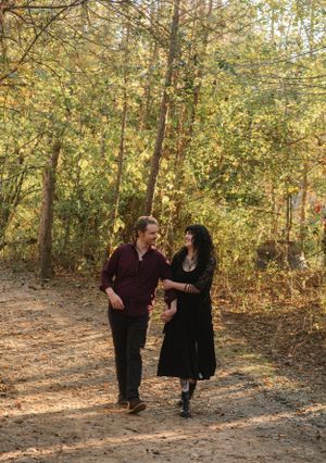 A couple walks together on a forest path surrounded by golden autumn foliage.