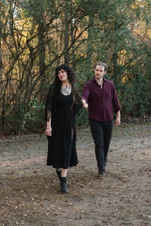 A couple takes a romantic stroll through an autumn forest path wearing dark clothing.