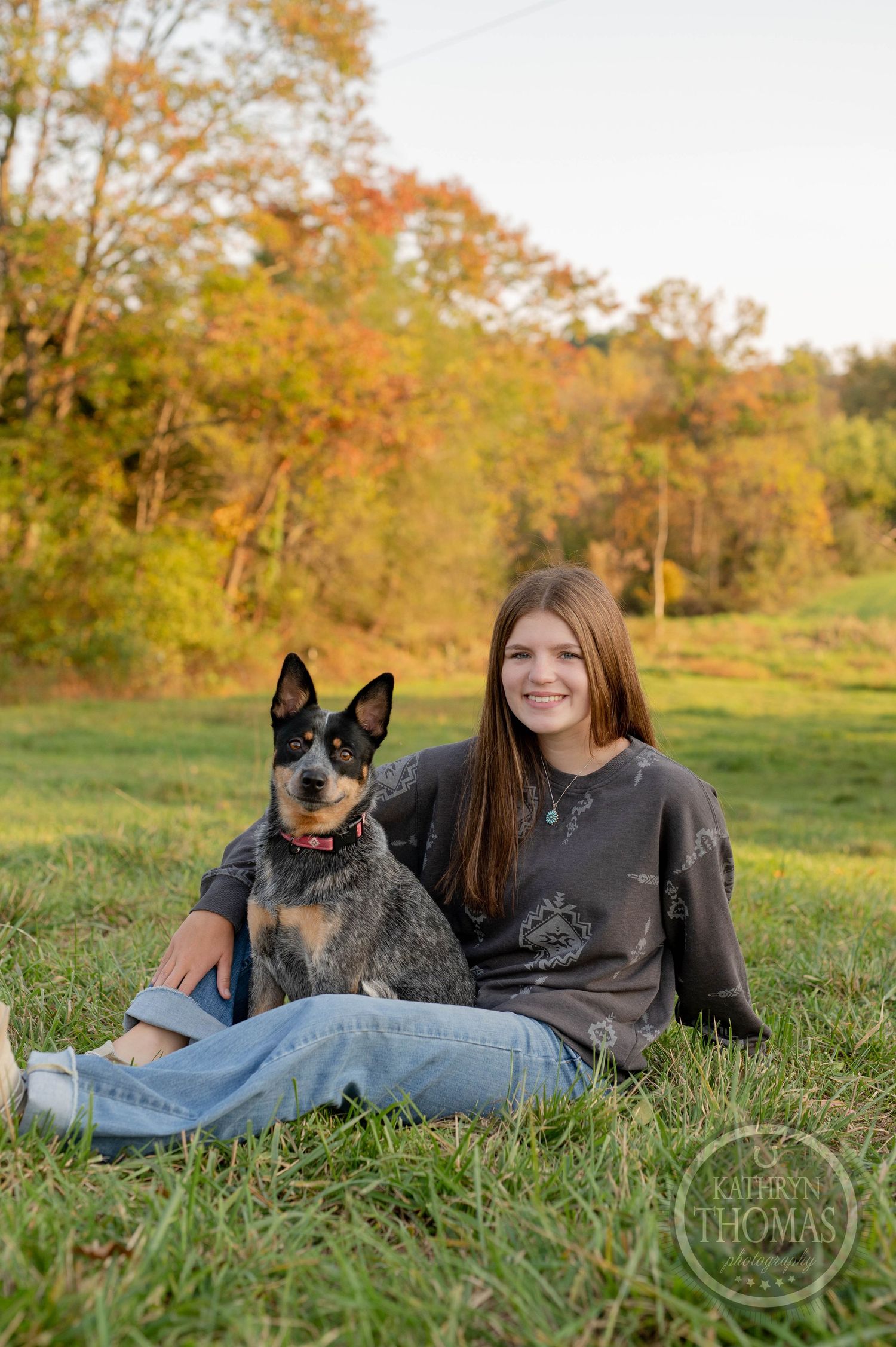 Person and Australian Cattle Dog relax together on grass in autumn setting.