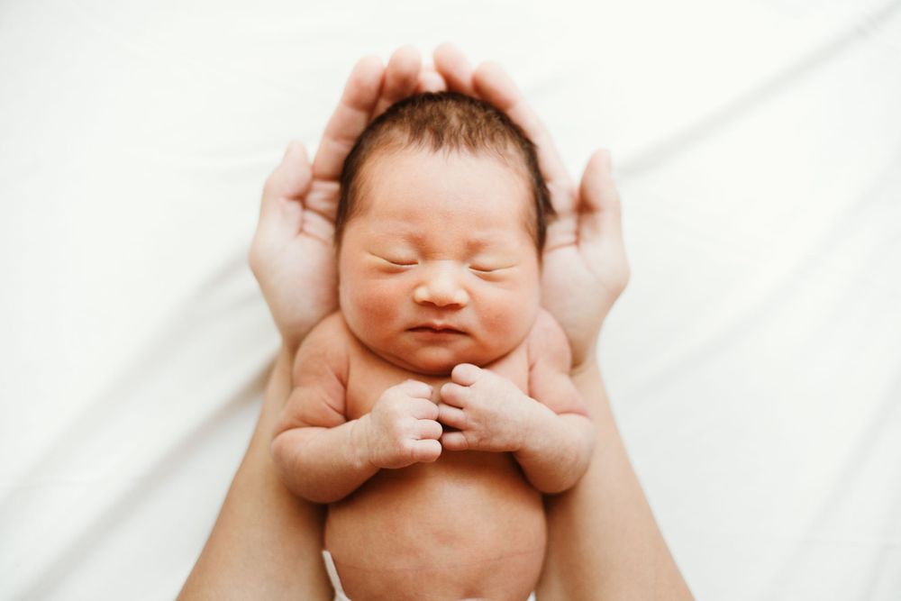Newborn baby lying on white blanket with hands cradling head.