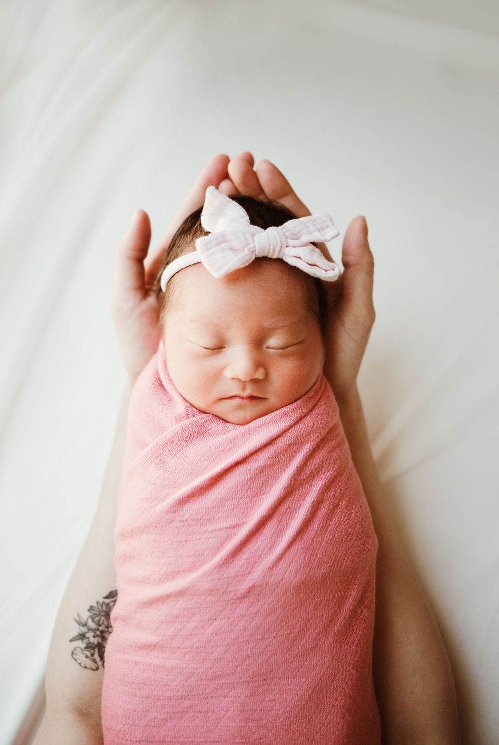 Sleeping newborn wrapped in pink swaddle wearing white bow headband.