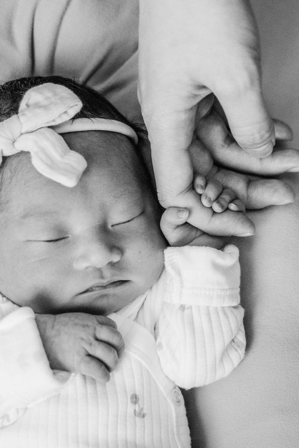 Newborn baby sleeps peacefully in white outfit with bow headband.